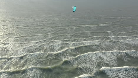 Kite-surfer-close-to-the-beach,-riding-the-wind-with-his-kite,-Drone-footage