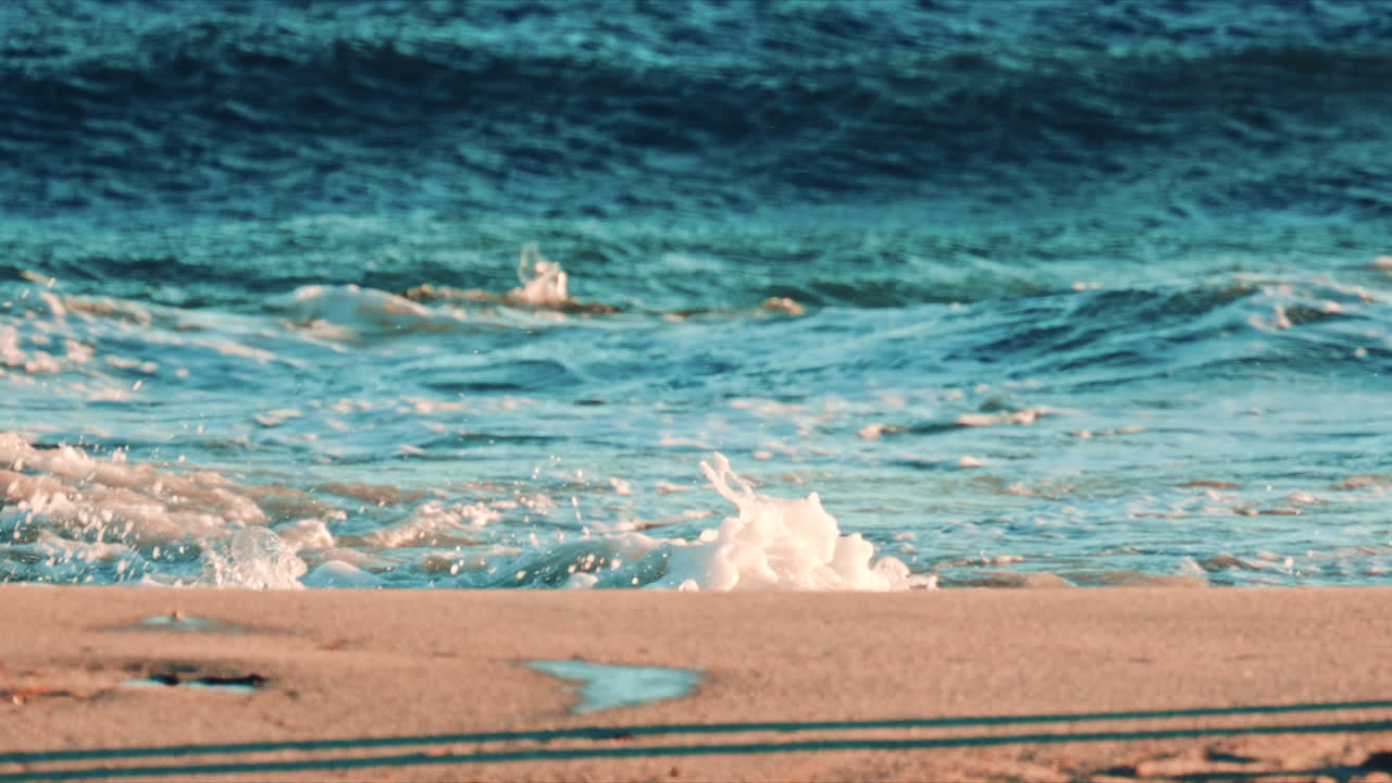 Close up of ocean foam washing over the sandy shore with deep blue waves behind it