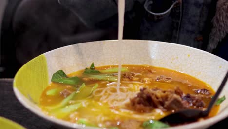 chopsticks lifting noodles from spicy broth