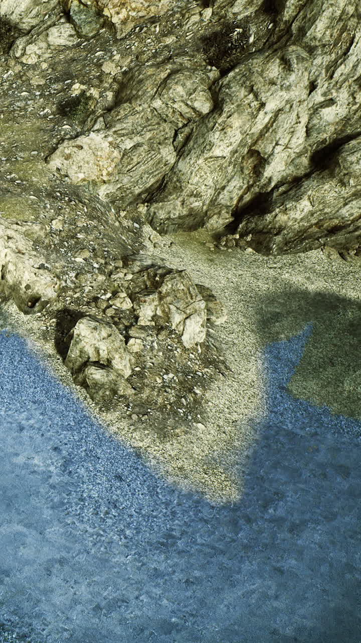 Rocky shoreline meets calm blue water during midday at the beach