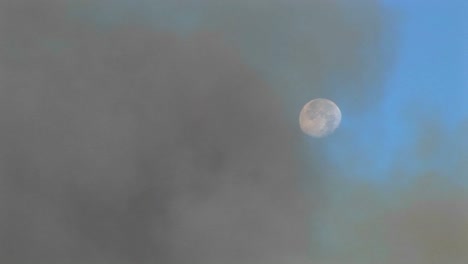 long shot of clouds of dark smoke clearing to reveal the moon in a blue sky