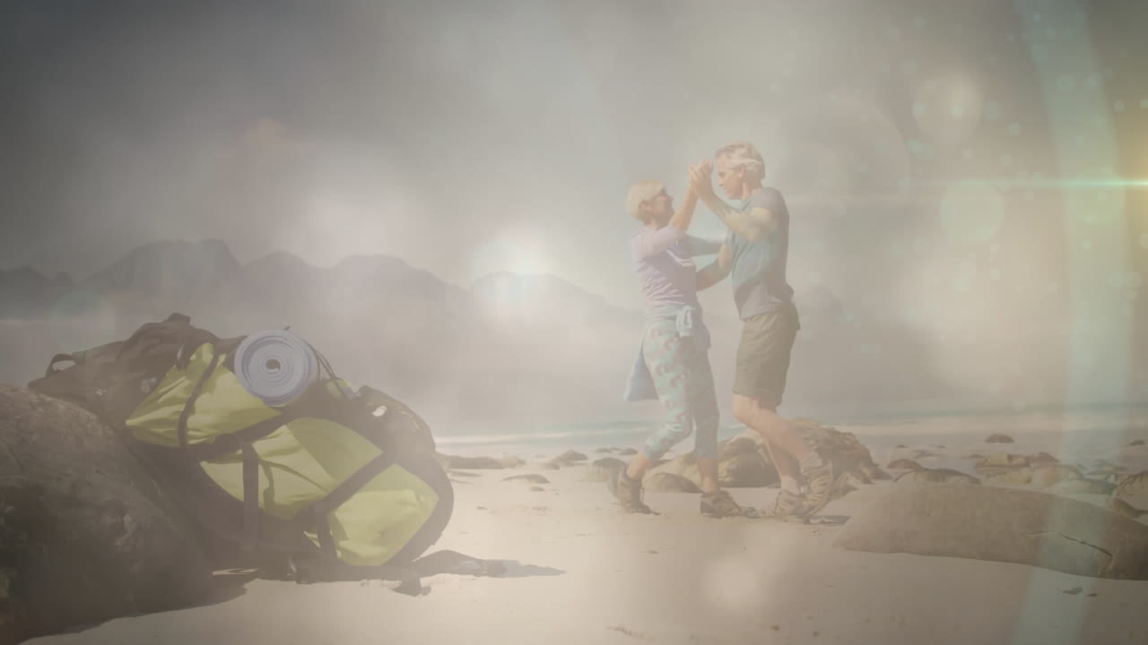 행복한 백인 노인 커플이 하이킹을 하고, 해변에서 춤을 추고, 빠르게 움직이는 구름과  ⁇ 빛 위에서