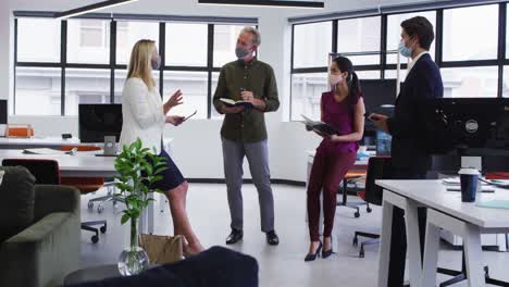 diverse business colleagues wearing face masks having casual meeting standing in office