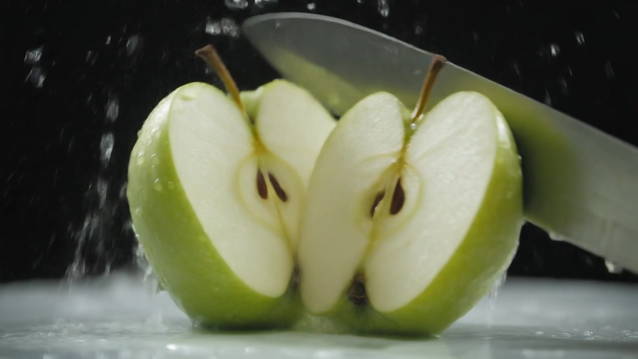 Coltello che affetta una mela verde fresca con schizzi d'acqua