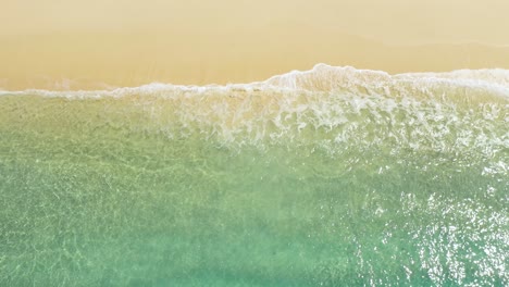 aerial view of clear turquoise waves on sandy beach at tropical island in indonesia