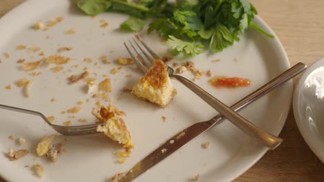 leftovers on a dirty plate with cutlery and herbs