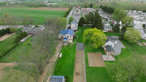 Un-Dron-Revela-Una-Granja-Serena-Con-Cultivos-En-Crecimiento,-Un-Acogedor-Parque-De-Casas-Móviles-Y-Los-Suaves-Tonos-De-La-Primavera