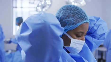 African-american-female-surgeon-wearing-surgical-cap,-putting-face-mask-on-in-operating-theatre