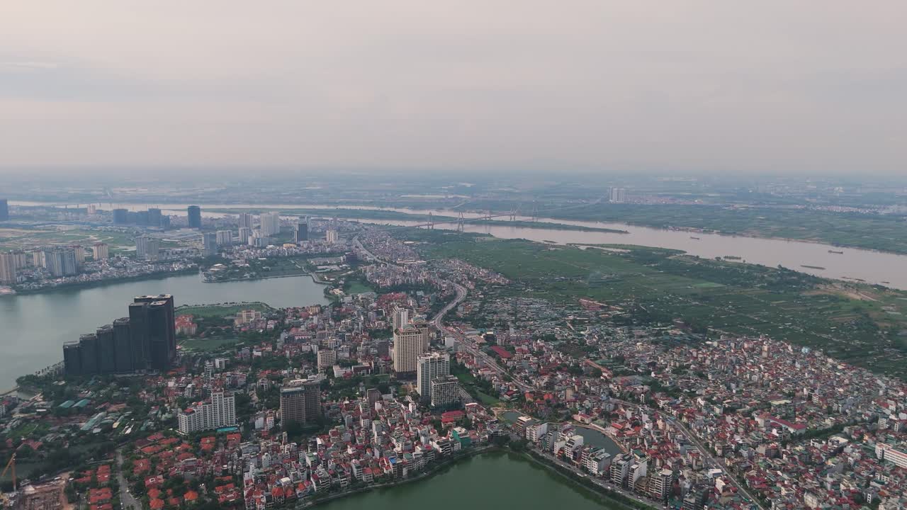 Expansive aerial view of Hanoi’s West Lake and Tay Ho district, blending water, modern buildings, and urban sprawl under soft daylight in Vietnam’s capital city
