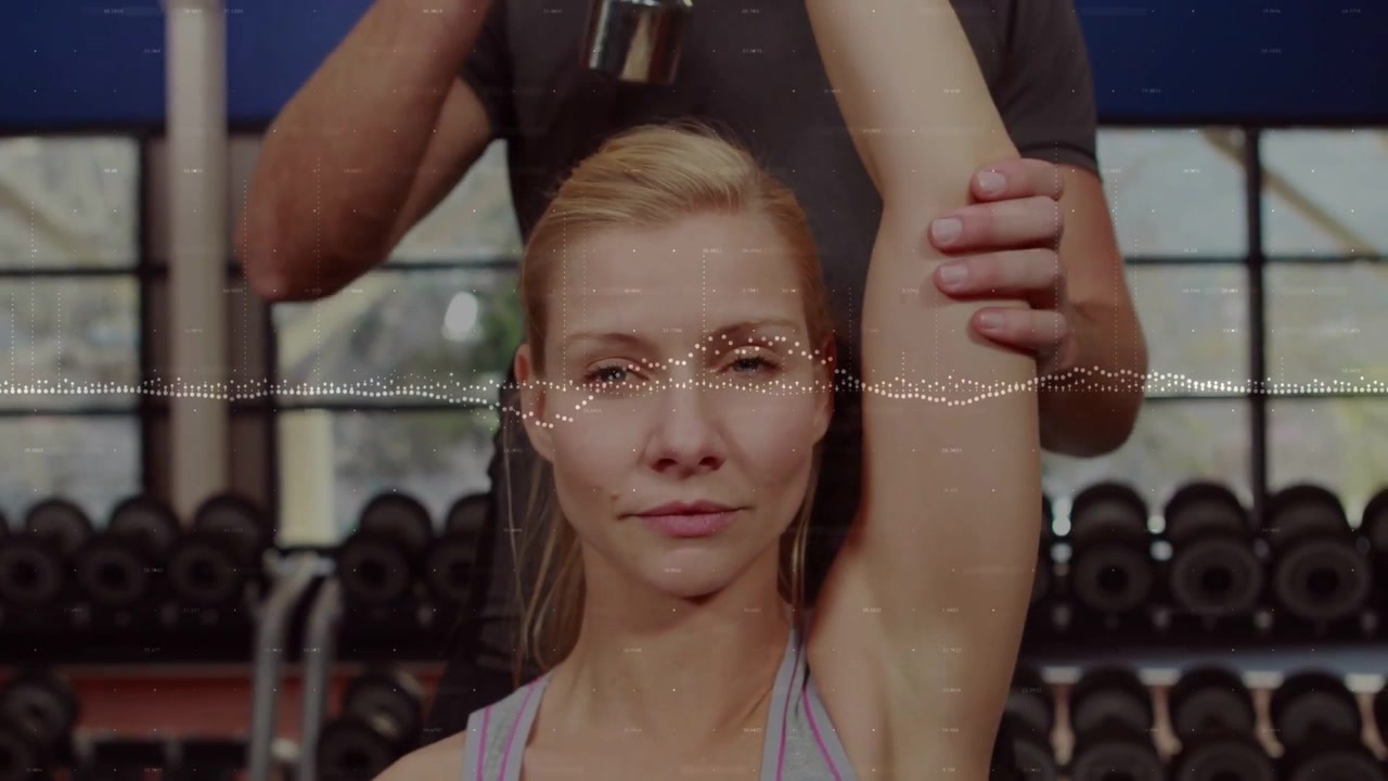 Spor salonunda sağ kolunu kaldıran müşteri, antrenör masajla gerginliği giderirken destekliyor, film greni efektiyle.
