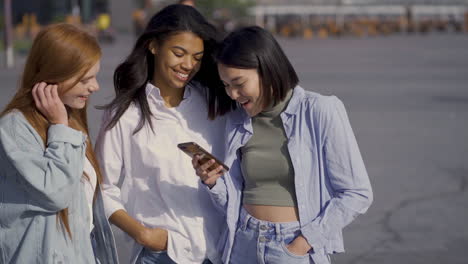 mujeres felices multiétnicas viendo algo en el teléfono al aire libre