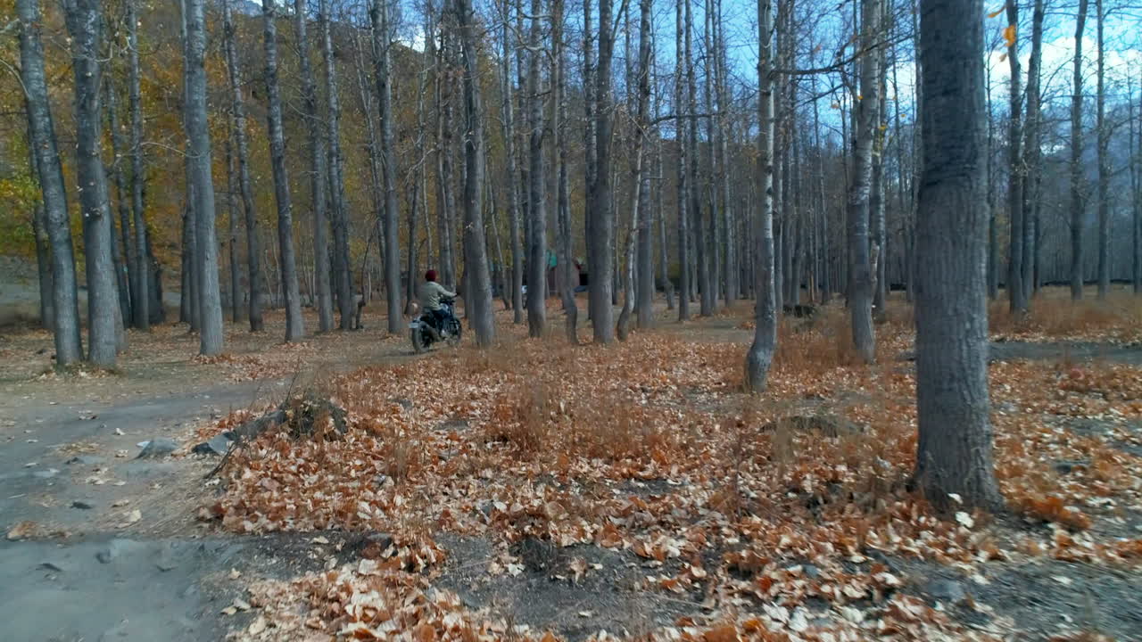 Cinematic back view of a man offroading on sports bike in the autumn woods surrounding a peaceful mountain valley.