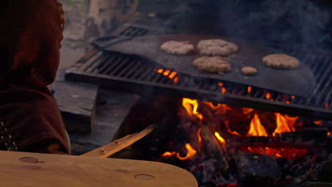 barbecue in medieval era, man in authentic clothes controlling the fire under meat on metal plate, slow motion