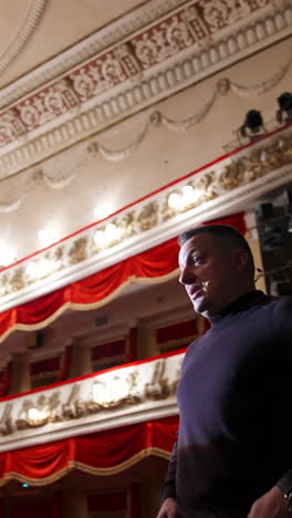 man is giving interview in the opera house. middle-aged actor talking to someone while standing on stage on classical theatre background. vertical video