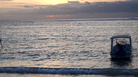 Slow-motion-mid-shot-of-a-boat-on-shore-at-sunset-on-a-beach-in-Nusa-Lembongan,-Indonesia