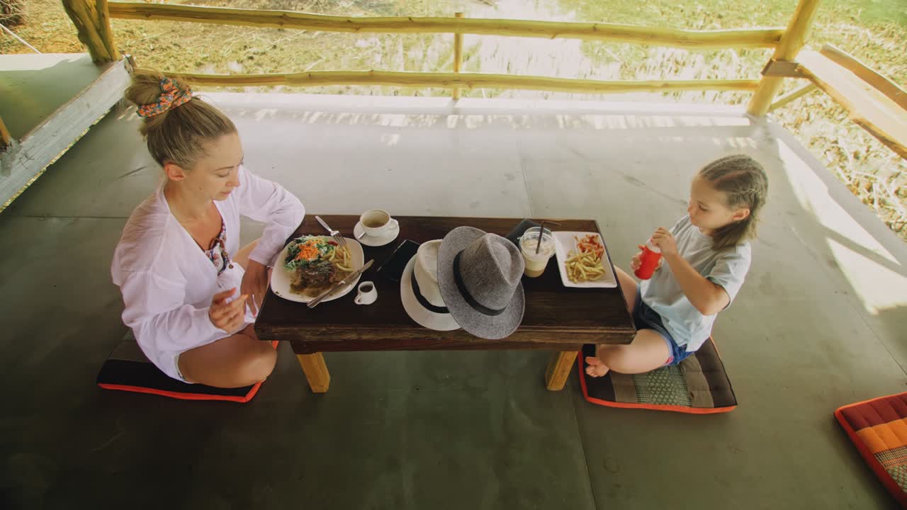 행복한 가족은 맛있는 음료를 먹고 마시며 물 위에 떠 있는 지역 카페에서 시간을 보내고 있습니다. 어머니와 딸은 야외에서 아침 식사를합니다.