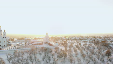 AERIAL:-Flying-above-the-car-driving-through-snowy-forest-at-golden-winter-sunrise.-People-on-winter-road-trip-traveling-across-snow-covered-Lapland-wilderness-at-sunset.-Car-driving-on-empty-icy-road