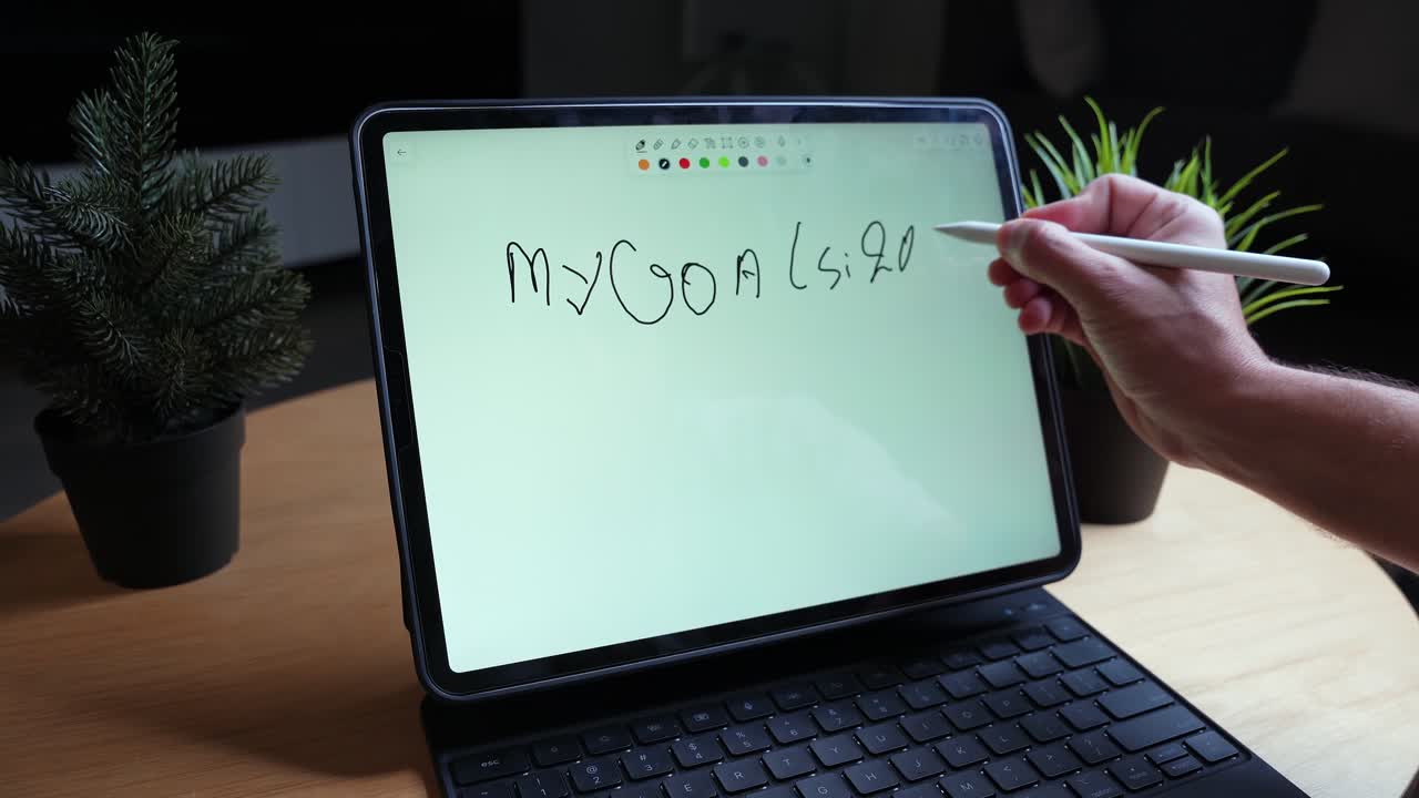 Close-up of hand using stylus to write “My Goals 2026” checklist on tablet with keyboard case at indoor desk, soft low light, productivity and goal-setting concept