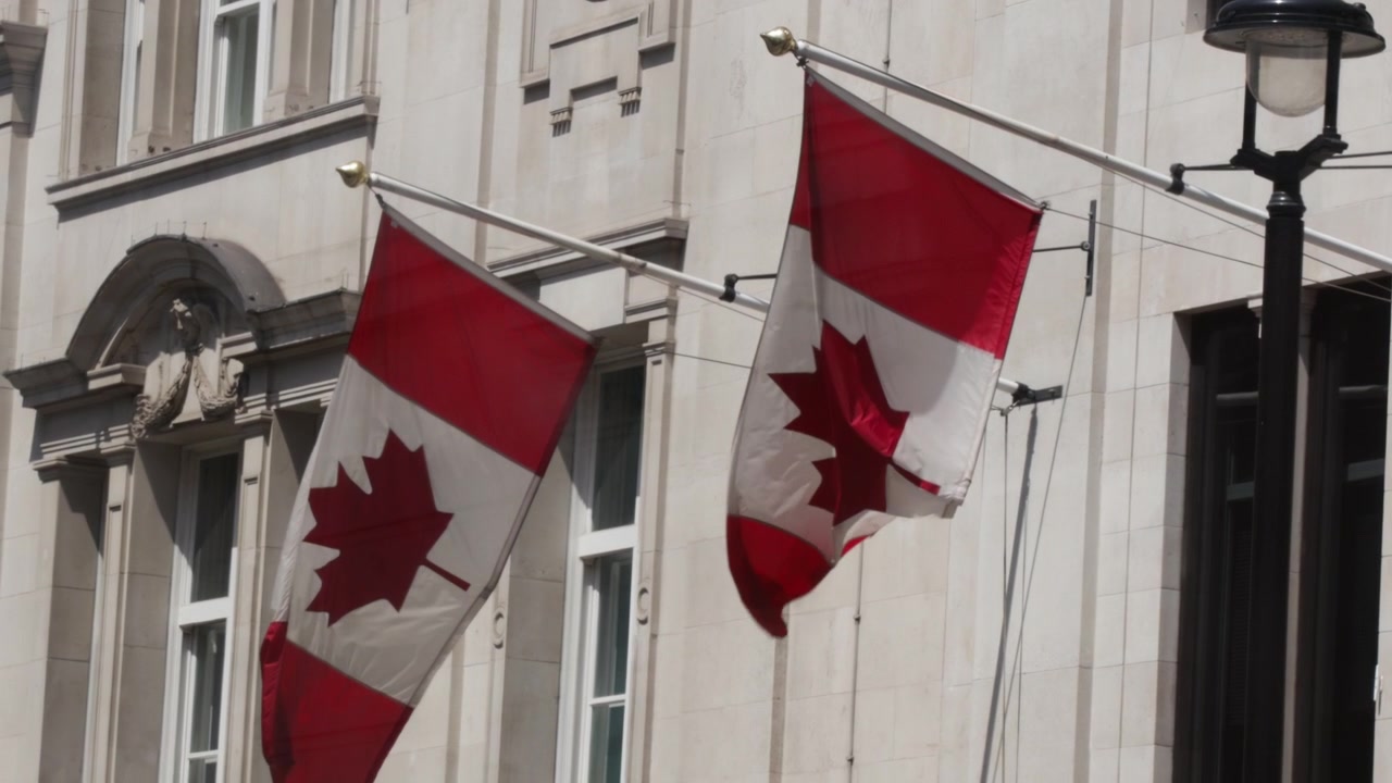 Bandiere canadesi sventolano fuori da un edificio storico nel centro di Londra in una giornata di sole.