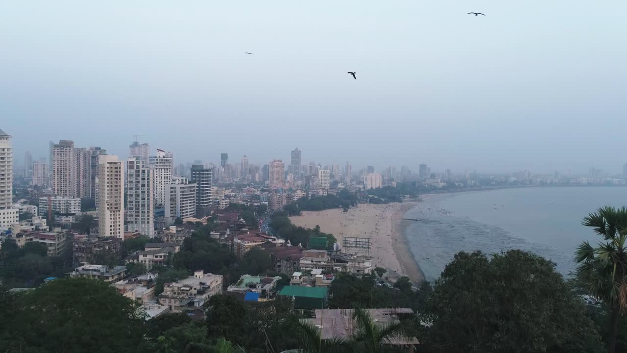uma tomada cinematográfica de drone do famoso ponto de praia de marine drive chaupati, na região sul de bombaim, na cidade de mumbai, com vista para a colina e a floresta do jardim suspenso em um movimento lento e suave