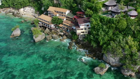 tropical-turquoise-ocean-coastline-in-Uluwatu-Bali-with-hotel-on-cliff,-aerial