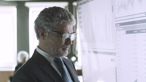 Experienced-grey-haired-CEO-checking-data-on-big-screen