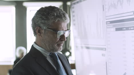 director ejecutivo de pelo gris con experiencia comprobando datos en pantalla grande