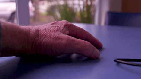 Close-up-of-a-caucasian-hand-and-thumb-tapping-on-a-blue-table,-shallow-depth-of-field