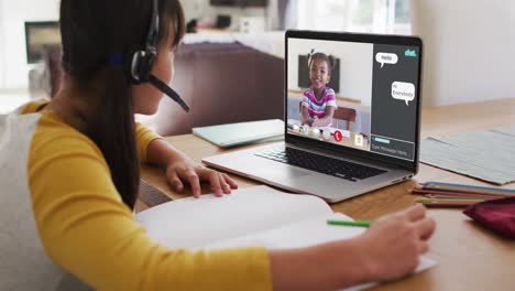 Schoolgirl-using-laptop-for-online-lesson-at-home,-with-girl-talking-and-web-chat-on-screen