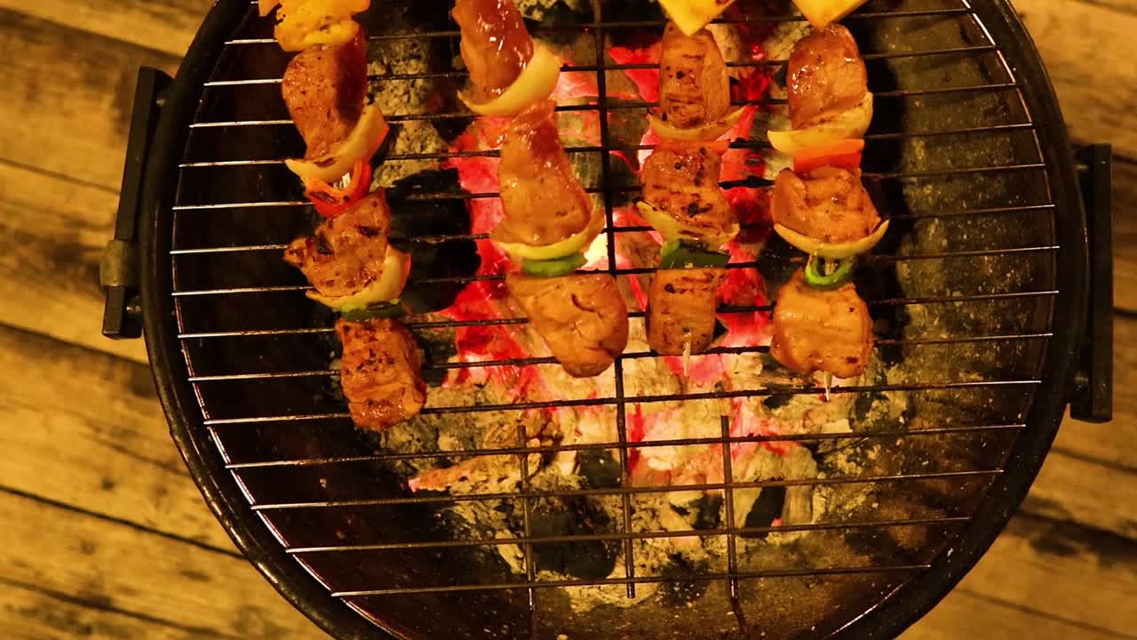 Close-up of vibrant skewers sizzling on a round grill with glowing coals beneath.