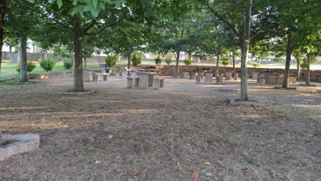 granite tables in a picnic area with barbecues under the oak trees in a public park on a sunny summer afternoon, rolling shot to the left