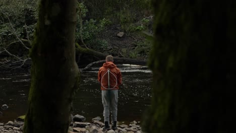 slow dolly shot framing a fisherman casting his spinner in between a tree trunk