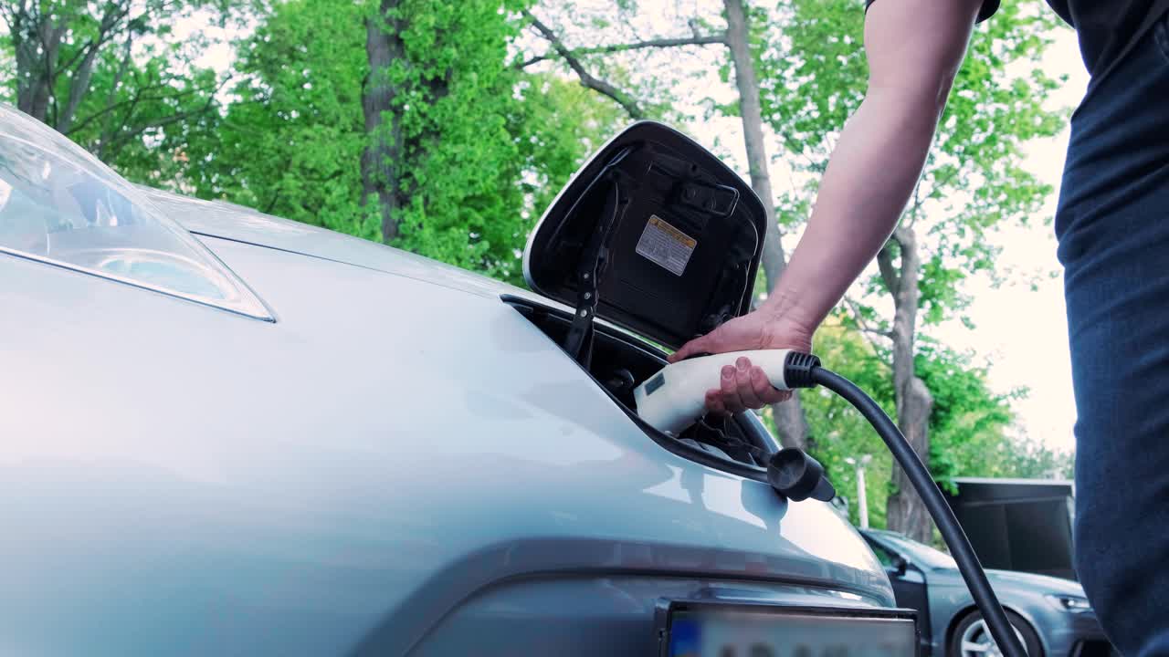 proceso de reabastecimiento de combustible de un automóvil eléctrico. un disparo debajo de la escotilla donde se carga el automóvil ecológico eléctrico. la escotella de carga del automóvil eléctrico se abre automáticamente. una mano masculina inserta un automóvil erecto