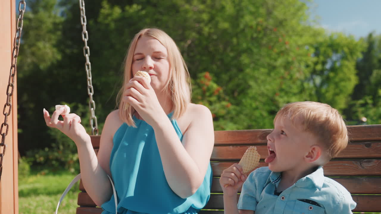 Zia bianca che gusta un gelato con un bambino su una panchina del parco durante un soleggiato fine settimana, assaporando lentamente, espressioni gioiose, brezza estiva, vestito blu casual, relax familiare spontaneo, momento del dessert