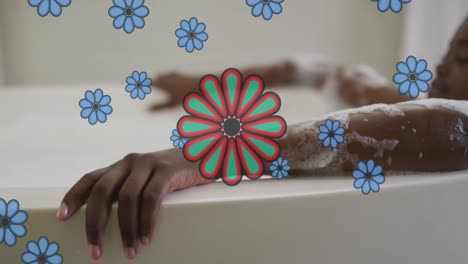 Animation-of-blue-flowers-over-happy-african-american-woman-relaxing-in-bath-at-home