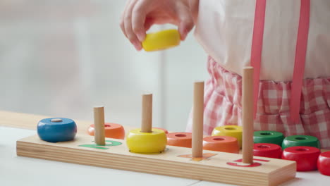 close-up van de hand van een meisje die kleurrijke ringen op houten kolommen stapelt - educatief speelgoedspel voor kinderen om getallen en tellen, sorteren, wiskunde en kleuren te leren