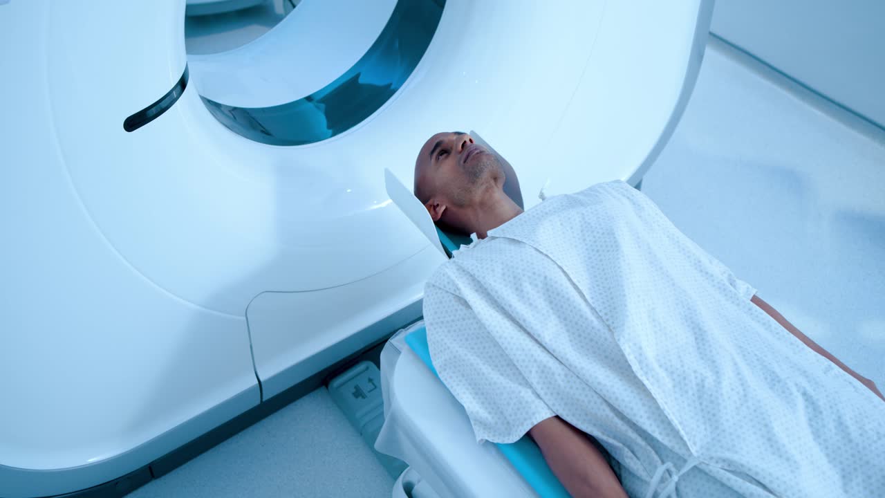 Paziente afroamericano di sesso maschile sdraiato su lettino medico che sposta la testa nello scanner, cuscino di gommapiuma per la scansione