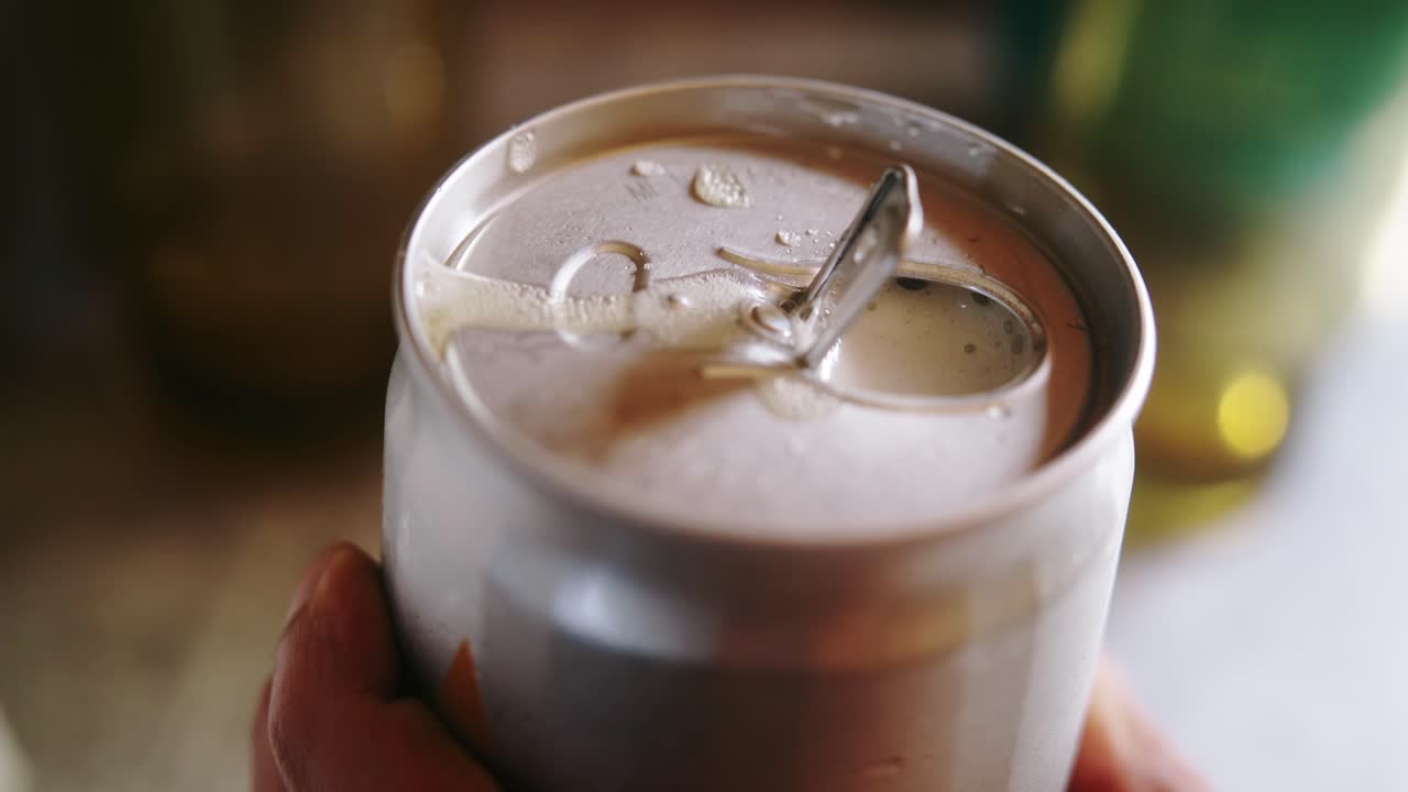 Close-up of a hand opening a soda can, capturing crisp detail of the tab lift and fizzy carbonation release. 30 fps