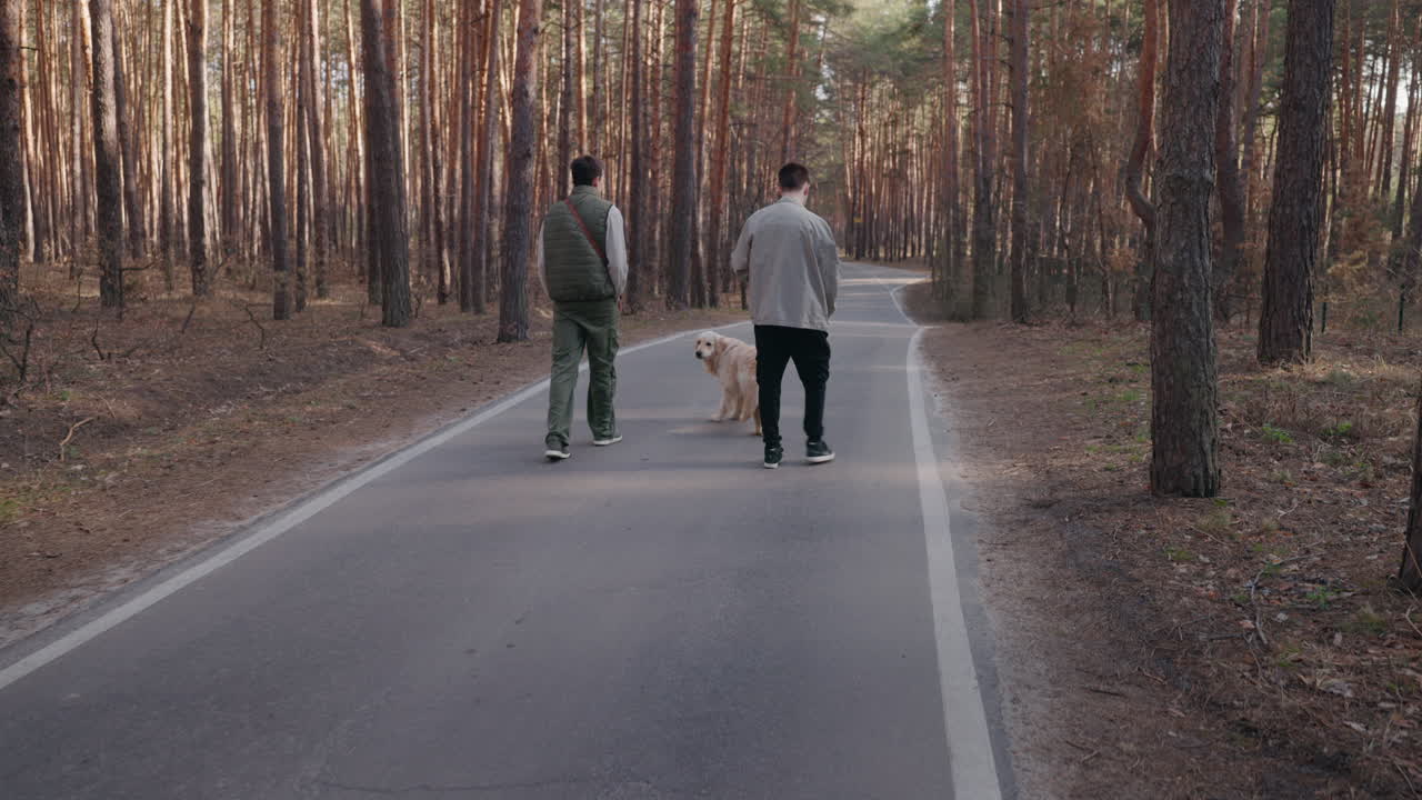 두 남자가 숲길에서 개를 산책시키고 있다.