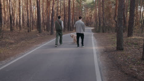 two men walking their dog on a forest road