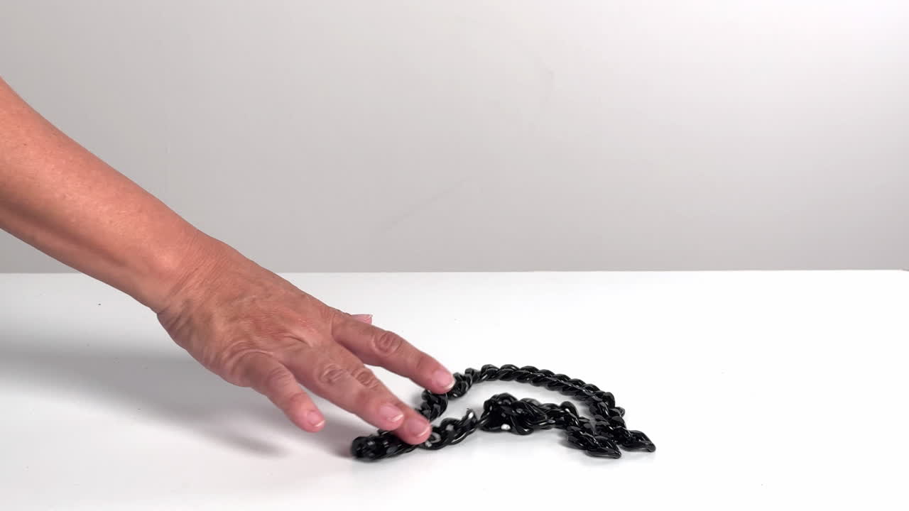 Mano che manipola una catena nera su una superficie bianca