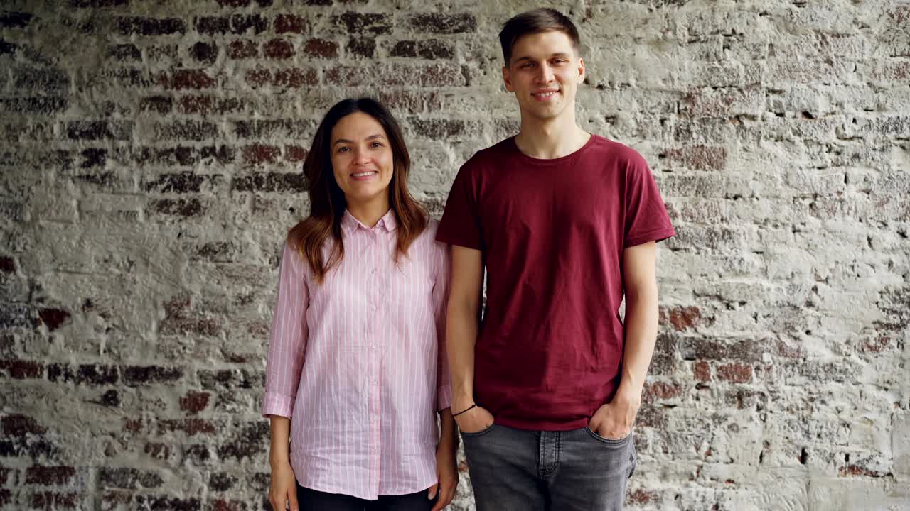 retrato de una atractiva pareja de raza mixta de pie juntos contra una pared de ladrillo mirando a la cámara y sonriendo. gente feliz y concepto interior moderno.