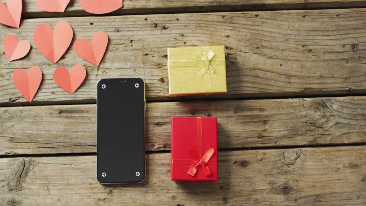 Paper hearts and smartphone with gifts on wooden background at valentine's day