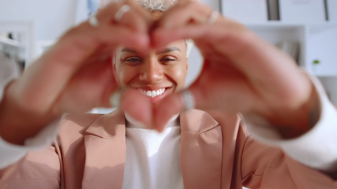 Young african american woman brings hands to camera with gesture heart