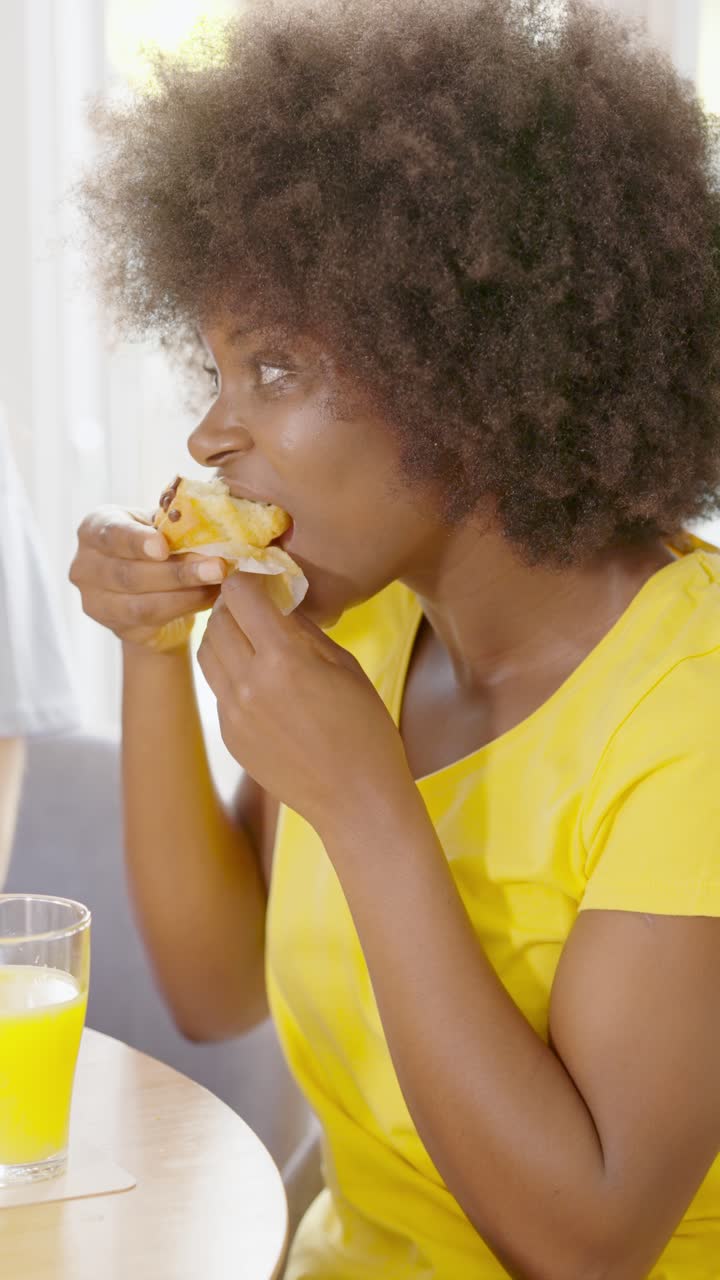 Woman with afro hair enjoying a pastry and juice