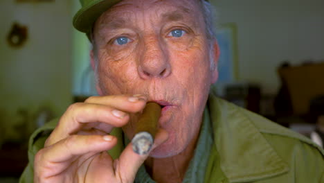 mature male in his 60s blowing cigar smoke directly at the camera