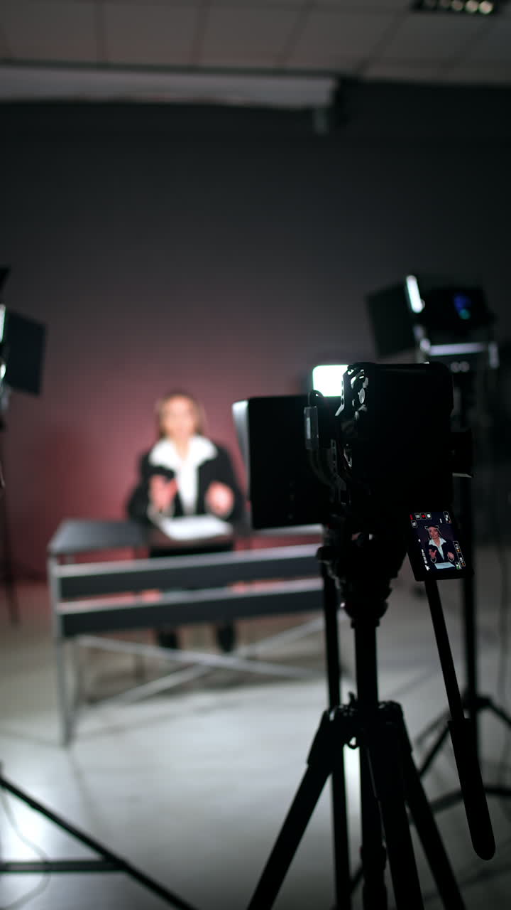 Camera on tripod works recording a video with a woman. Unrecognized woman standing beside takes video on her phone. Blurred backdrop. Vertical video