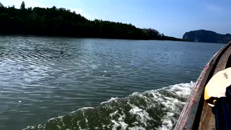 traditional longtail boat sailing on gulf of thailand, passenger pov of bow wave and scenic coastline