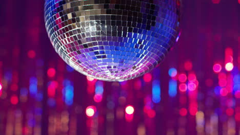 close up of mirrorball slowly revolving in night club or disco with sparkling lights in background