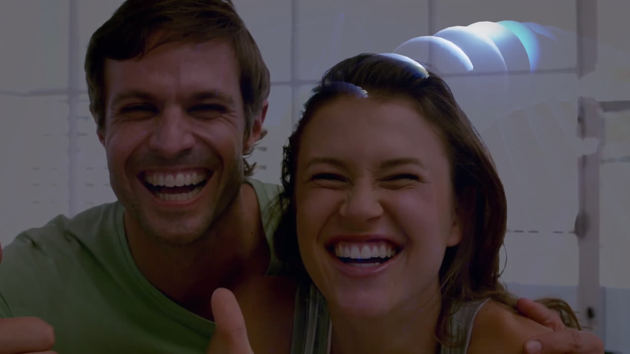 Pareja haciendo el gesto de 'pulgar arriba' en el interior de una casa, mostrando tecnología con círculos de datos azules brillantes.